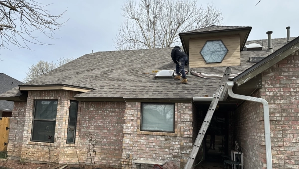 GC LLC painter repairing and painting exterior roof trim on a brick home in Edmond, OK